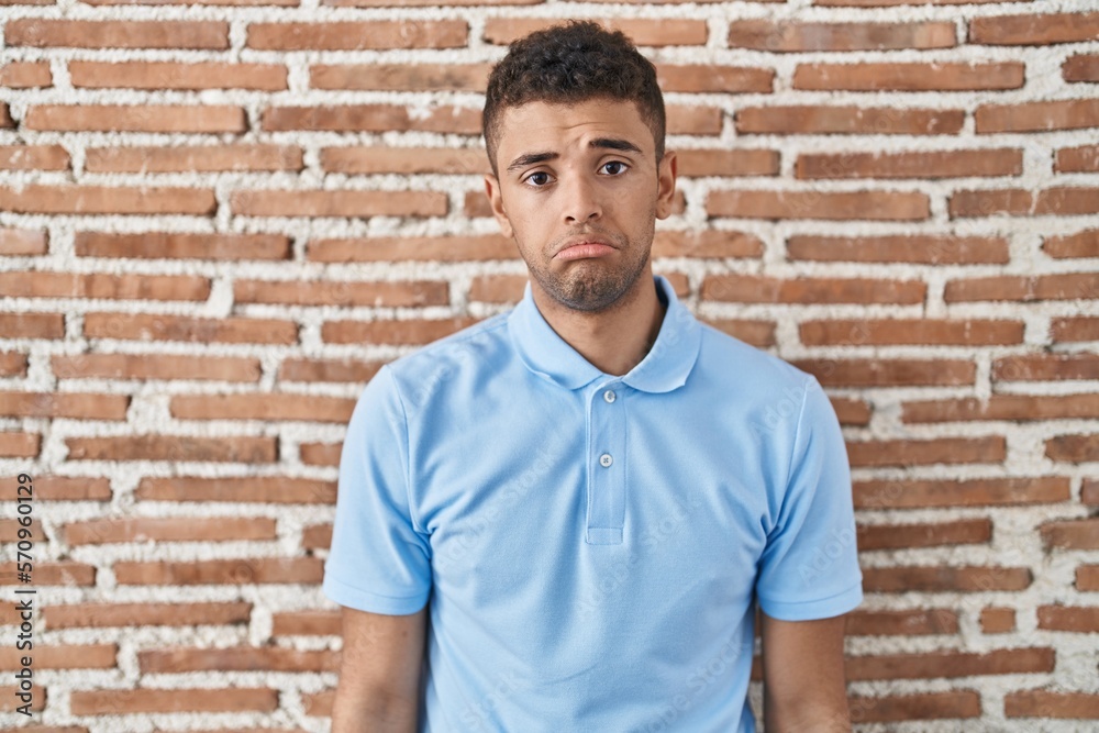 Brazilian young man standing over brick wall depressed and worry for distress, crying angry and afraid. sad expression. Brazilian young man standing over brick wall depressed and worry for distress, crying angry and afraid. sad expression.