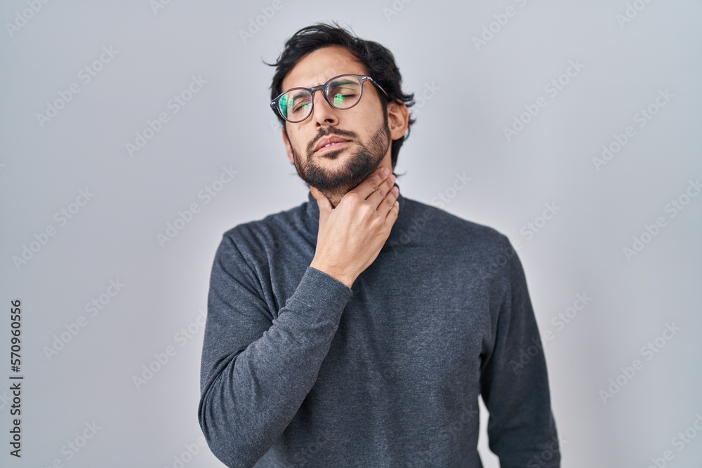 Handsome latin man standing over isolated background touching painful neck, sore throat for flu, clod and infection