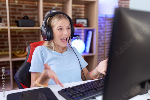 Young caucasian woman playing video games wearing headphones smiling cheerful with open arms as friendly welcome, positive and confident greetings