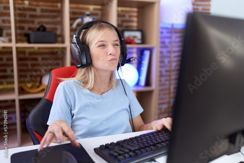 Young caucasian woman playing video games wearing headphones looking at the camera blowing a kiss on air being lovely and sexy. love expression.