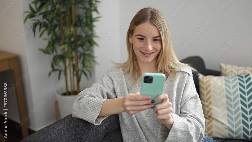 Young blonde woman using smartphone sitting on the sofa at home Young blonde woman using smartphone sitting on the sofa at home