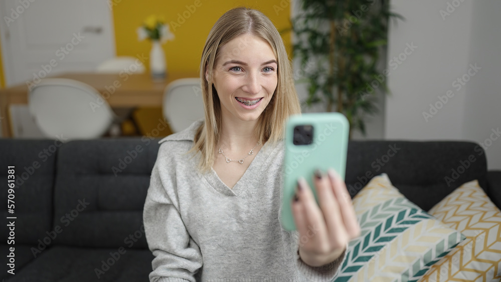 Young blonde woman taking selfie picture with smartphone sitting on the sofa at home Young blonde woman taking selfie picture with smartphone sitting on the sofa at home