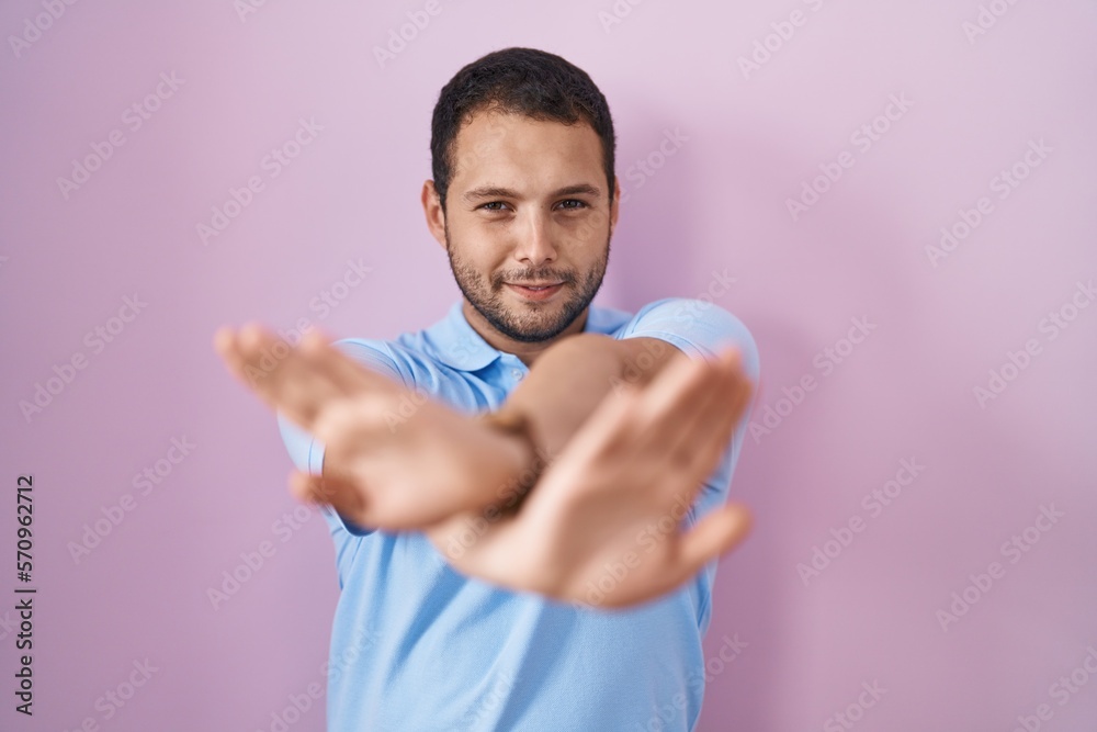 Hispanic man standing over pink background rejection expression crossing arms and palms doing negative sign, angry face Hispanic man standing over pink background rejection expression crossing arms and palms doing negative sign, angry face