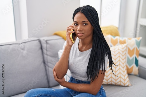 African american woman talking on smartphone with serious expression at home