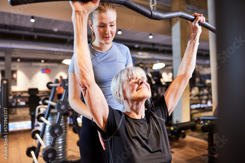 gym instructor helping a senior woman lifting weights. Trainer helping a smiling senior lift weights. Senior woman exercising with personal trainer