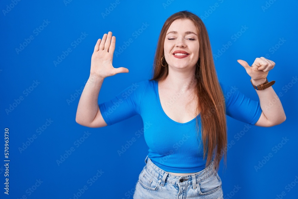 Fototapeta premium Redhead woman standing over blue background showing and pointing up with fingers number six while smiling confident and happy.