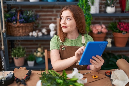 Young redhead woman florist smiling confident using touchpad at flower shop