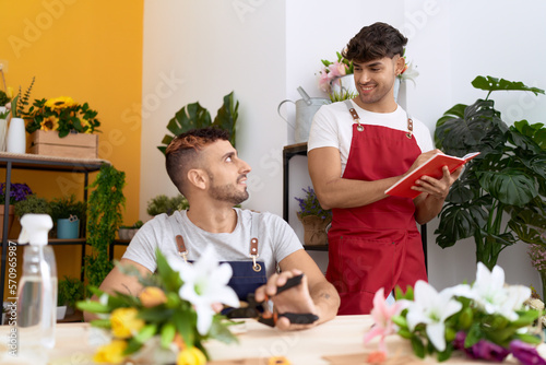 Two hispanic men florists cutting stem of flower writing on notebook at flower shop