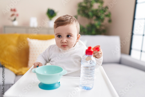 Adorable caucasian baby sitting on highchair eating biscuit at home