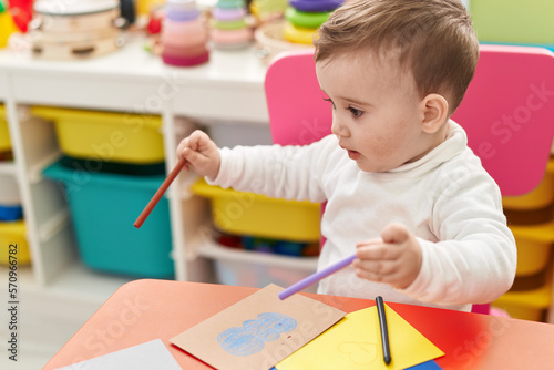 Adorable caucasian baby student sitting on table drawing on paper at kindergarten