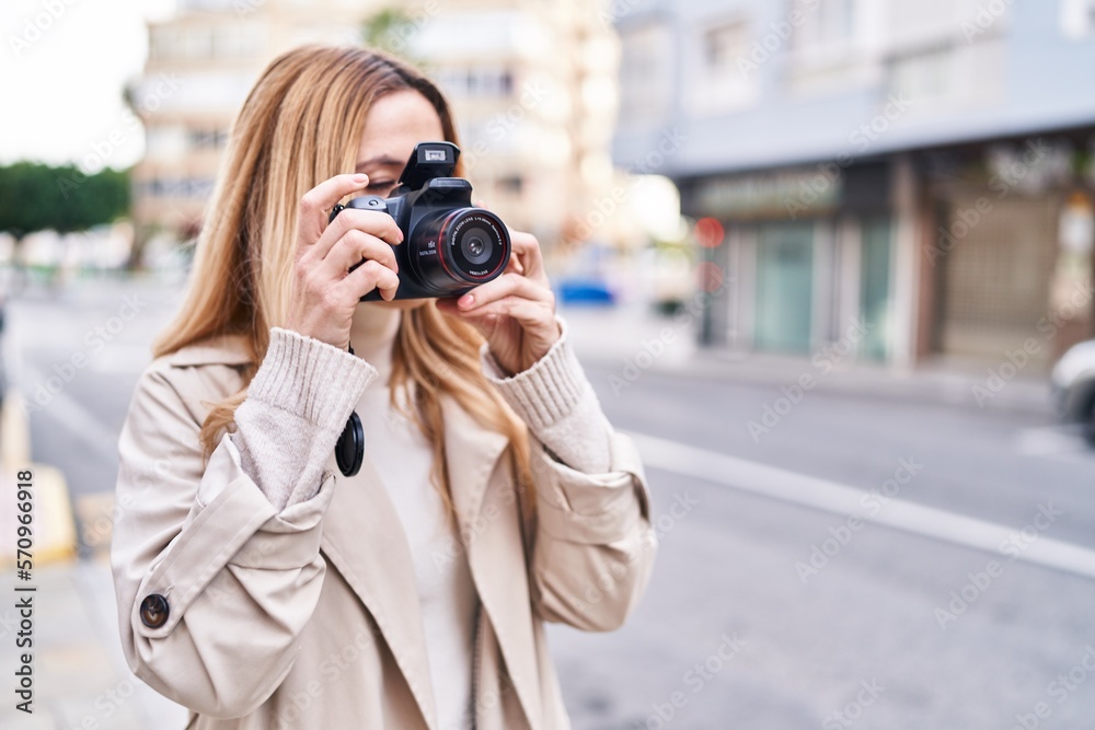 Young blonde woman susing professional camera at street