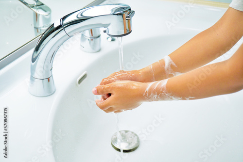手あらいをした泡を流水で洗い流す幼児の手