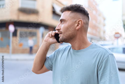 Young hispanic man talking on smartphone with serious expression at street