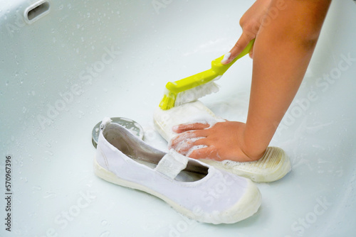 洗面台で自分の上靴の底をブラシで綺麗に磨いて家事を手伝う幼児の手 photo