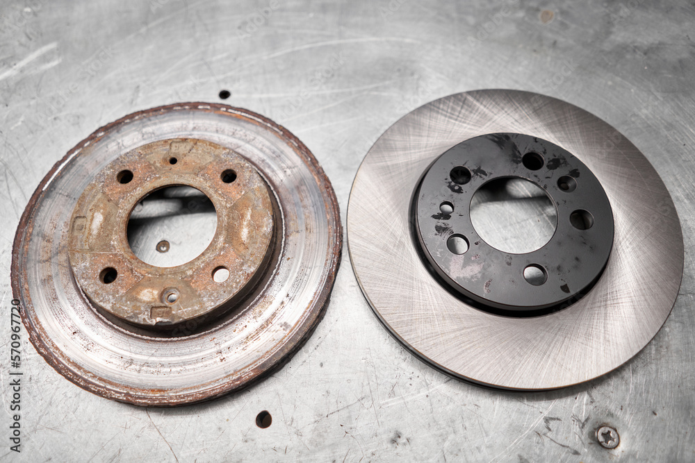 Old rusty brake disc and new disc. Change the old to new brake disc on car in a garage. Auto repair concept. Old rusty brake disc and new disc. Change the old to new brake disc on car in a garage. Auto repair concept.