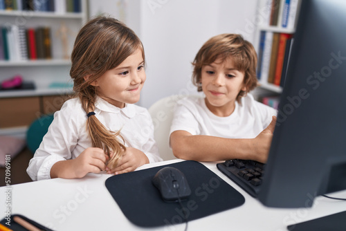 Brother and sister students using computer sitting on table at classroom