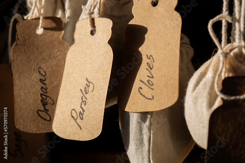 Herbs in jute bags sacks, parsley, sage, oregano and cloves, hanging on metal hooks in a kitchen. labelled with card tags