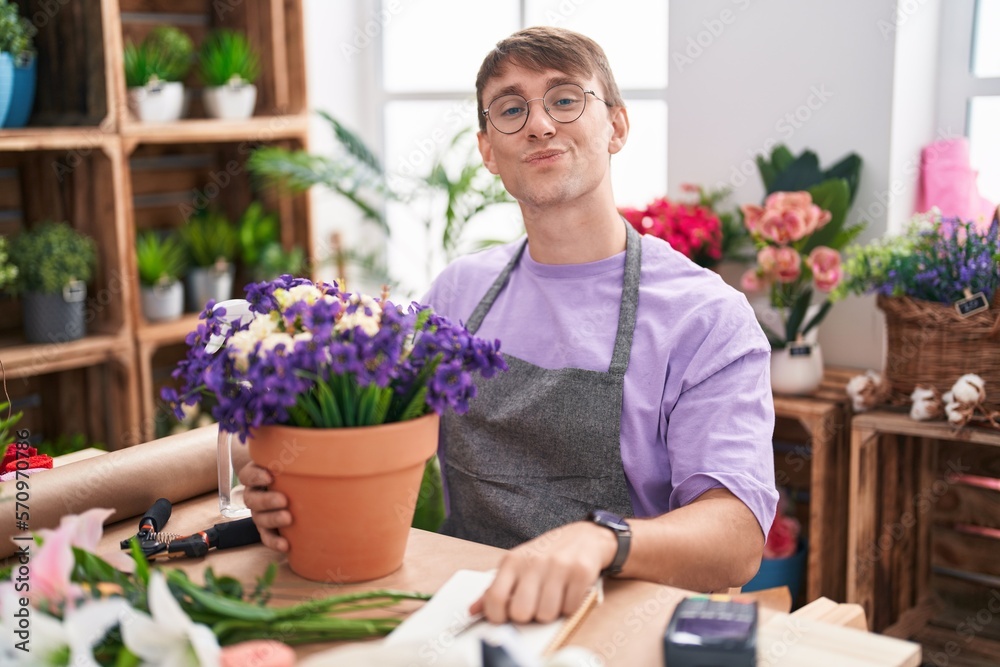Caucasian blond man working at florist shop looking at the camera blowing a kiss on air being lovely and sexy. love expression.
