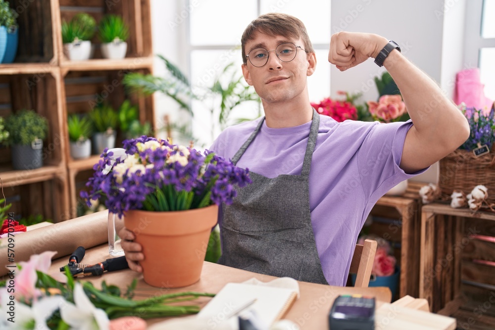 Caucasian blond man working at florist shop strong person showing arm muscle, confident and proud of power