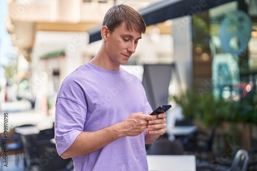 Young caucasian man using smartphone with serious expression at coffee shop terrace © Krakenimages.com