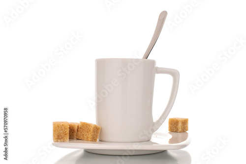 Several cubes of brown sugar with ceramic white cup with saucer and metal spoon, macro, isolated on white background.