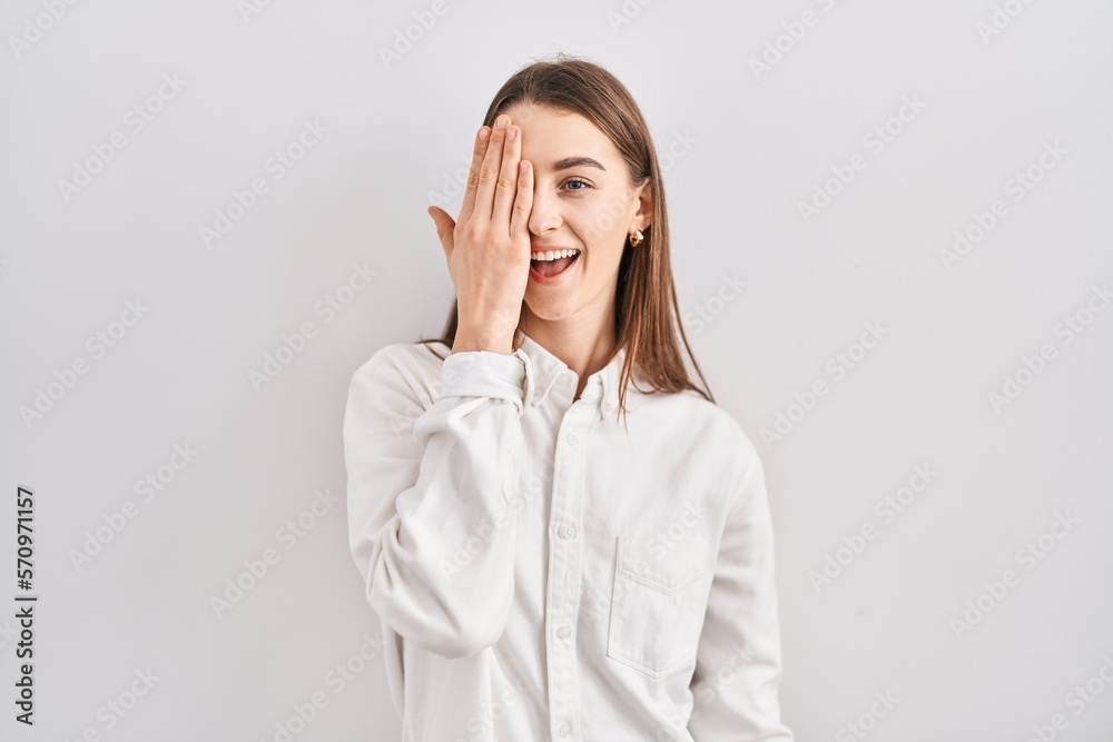 Young caucasian woman standing over isolated background covering one eye with hand, confident smile on face and surprise emotion. Young caucasian woman standing over isolated background covering one eye with hand, confident smile on face and surprise emotion.