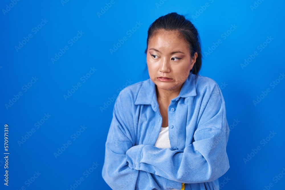 Asian young woman standing over blue background shaking and freezing for winter cold with sad and shock expression on face Asian young woman standing over blue background shaking and freezing for winter cold with sad and shock expression on face