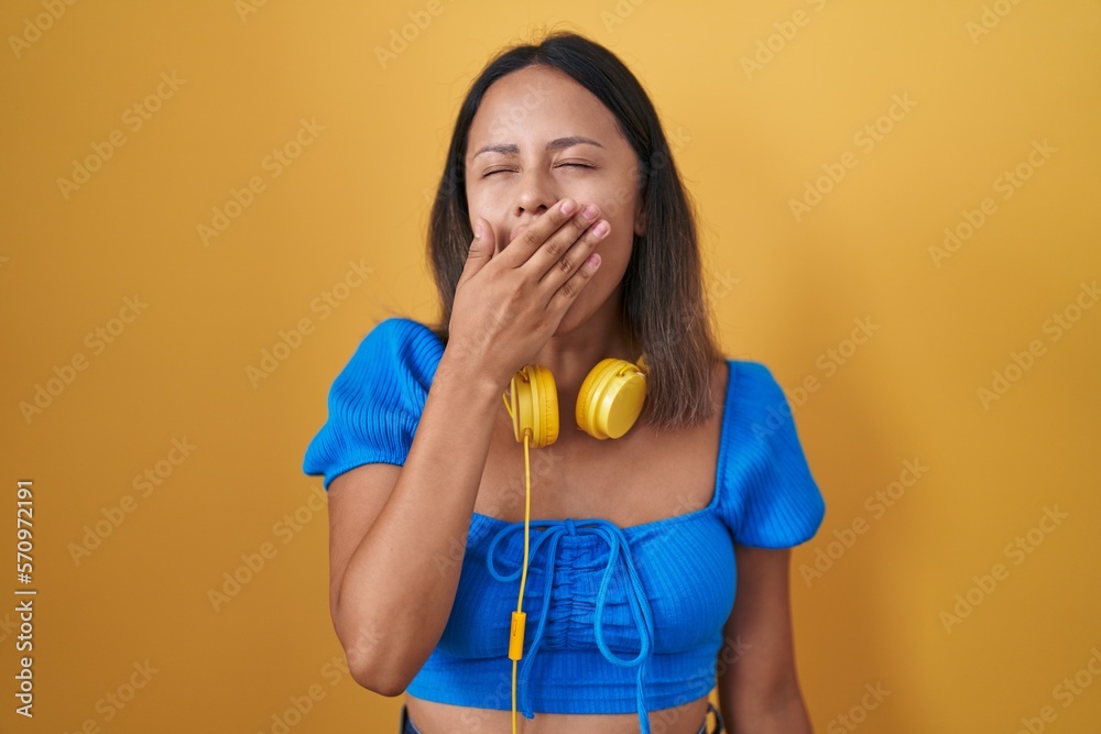 Hispanic young woman standing over yellow background bored yawning tired covering mouth with hand. restless and sleepiness. Hispanic young woman standing over yellow background bored yawning tired covering mouth with hand. restless and sleepiness.