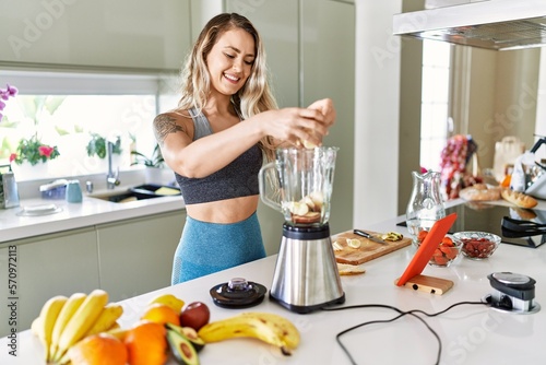 Young woman looking online juice recipe pouring banana on blender at kitchen