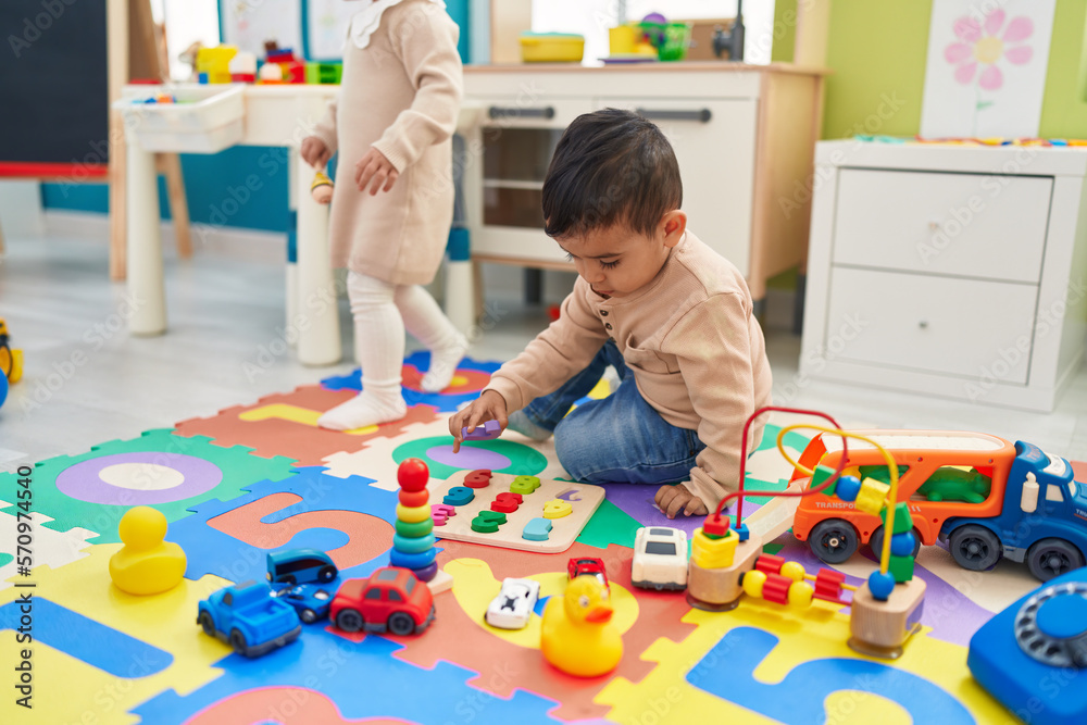 Fototapeta premium Two kids playing with maths puzzle game sitting on floor at kindergarten