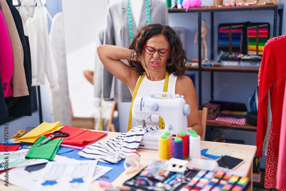 Fototapeta premium Middle age woman tailor stressed using sewing machine at clothing factory