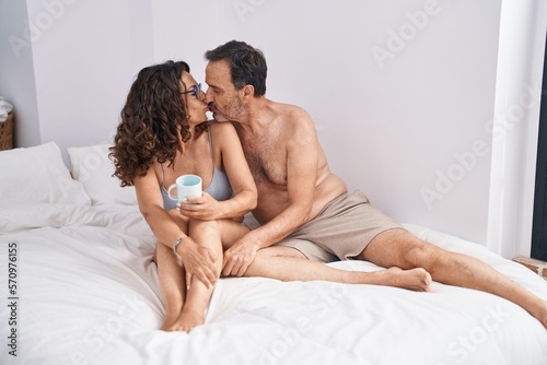Man and woman couple drinking cup of coffee sitting on bed at bedroom