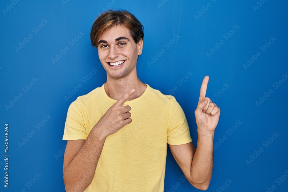 Young man standing over blue background smiling and looking at the camera pointing with two hands and fingers to the side. Young man standing over blue background smiling and looking at the camera pointing with two hands and fingers to the side.
