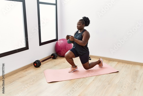 Young african american woman training using dumbbell at sport center