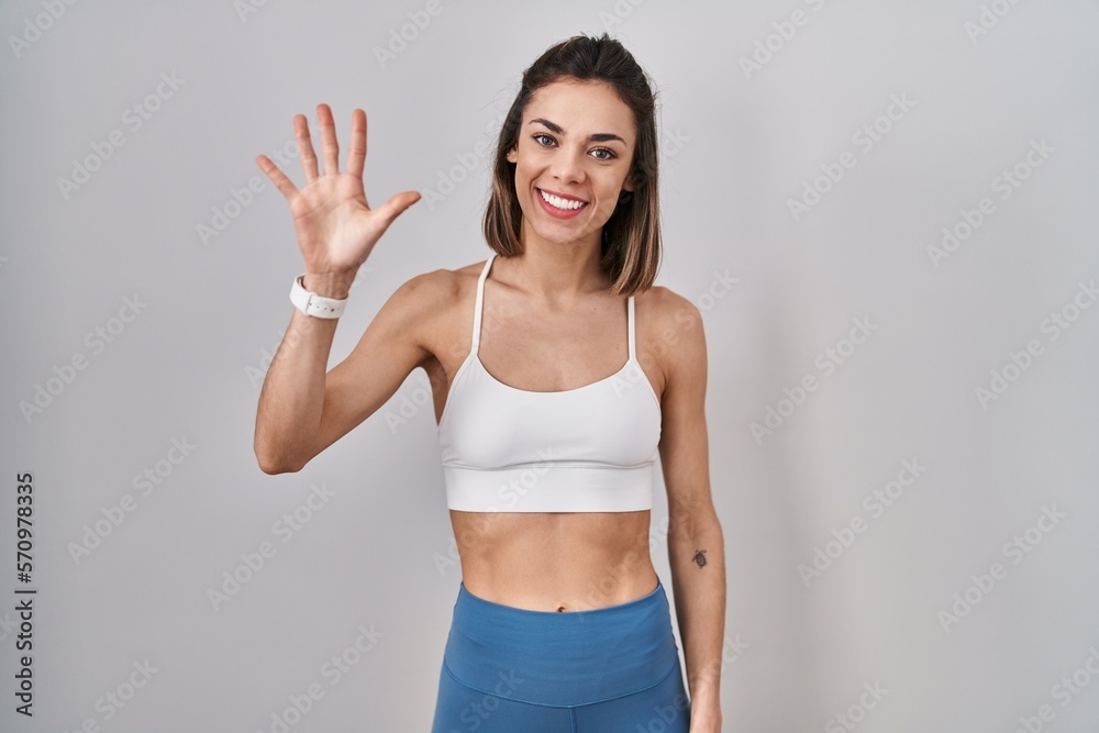 Hispanic woman wearing sportswear over isolated background showing and pointing up with fingers number five while smiling confident and happy.