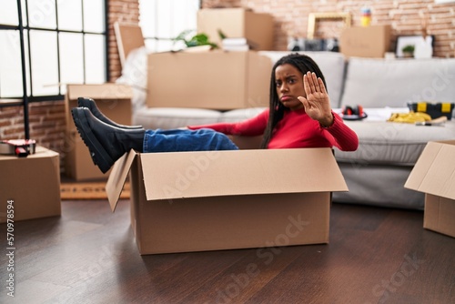 Young african american with braids moving to a new home inside of a cardboard box with open hand doing stop sign with serious and confident expression, defense gesture © Krakenimages.com