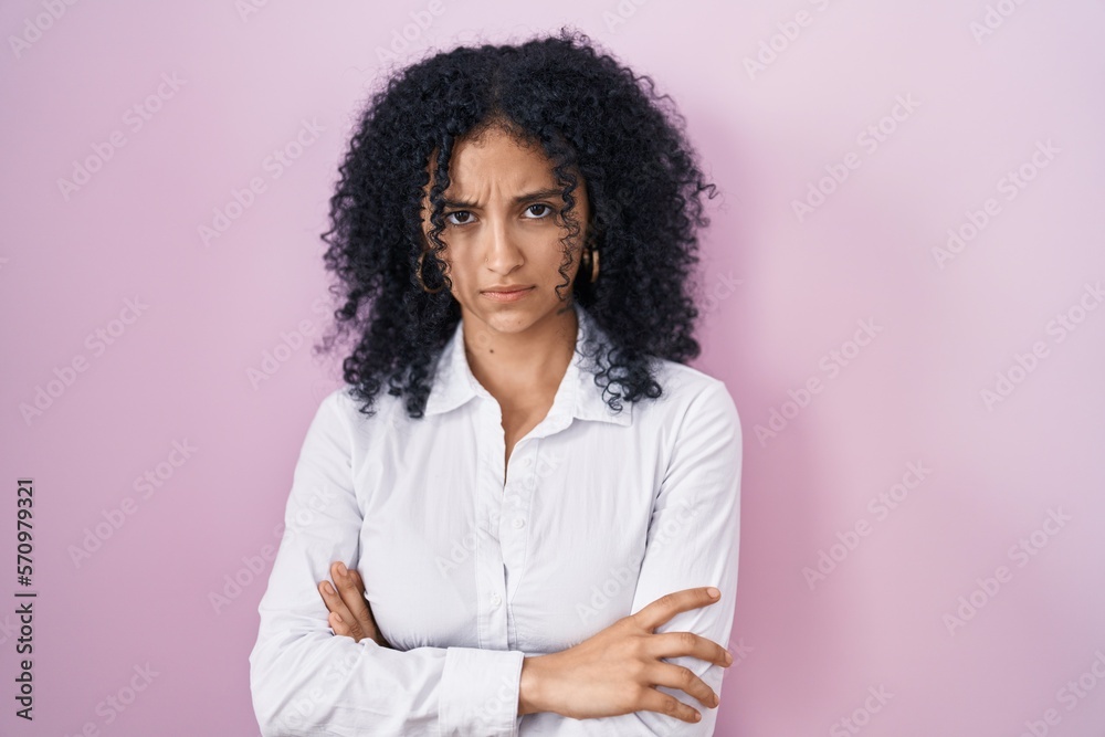 Hispanic woman with curly hair standing over pink background skeptic and nervous, disapproving expression on face with crossed arms. negative person. Hispanic woman with curly hair standing over pink background skeptic and nervous, disapproving expression on face with crossed arms. negative person.