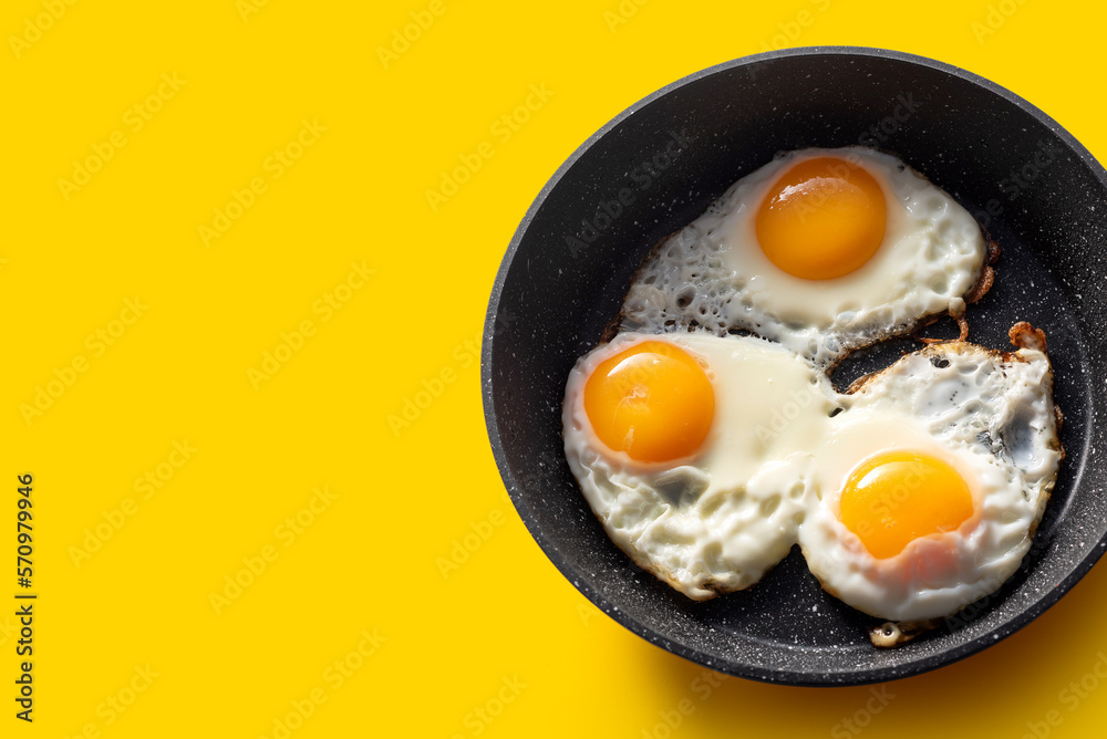 Frying pan with scrambled eggs from 3 eggs on a yellow background Frying pan with scrambled eggs from 3 eggs on a yellow background