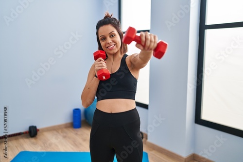 Young beautiful hispanic woman smiling confident using dumbbells boxing at sport center