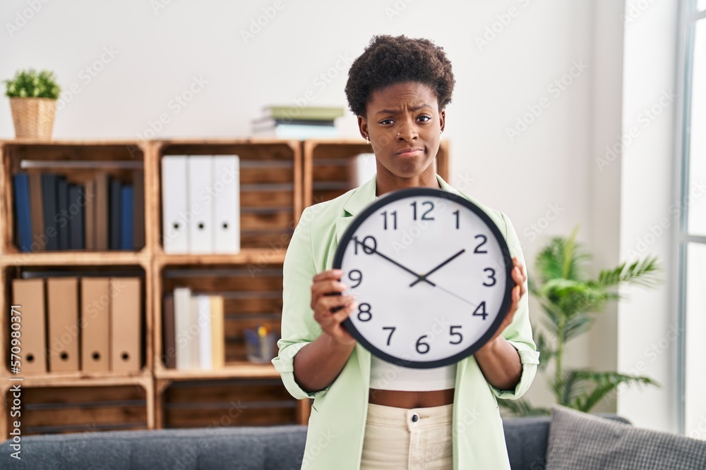 African american woman holding big clock skeptic and nervous, frowning upset because of problem. negative person. African american woman holding big clock skeptic and nervous, frowning upset because of problem. negative person.