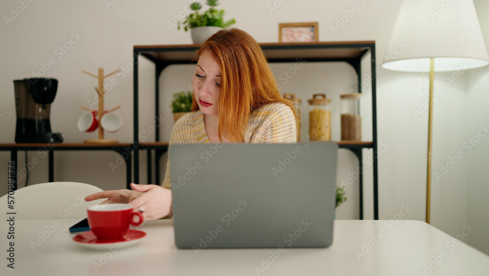 Young redhead woman using laptop drinking coffee at home Young redhead woman using laptop drinking coffee at home
