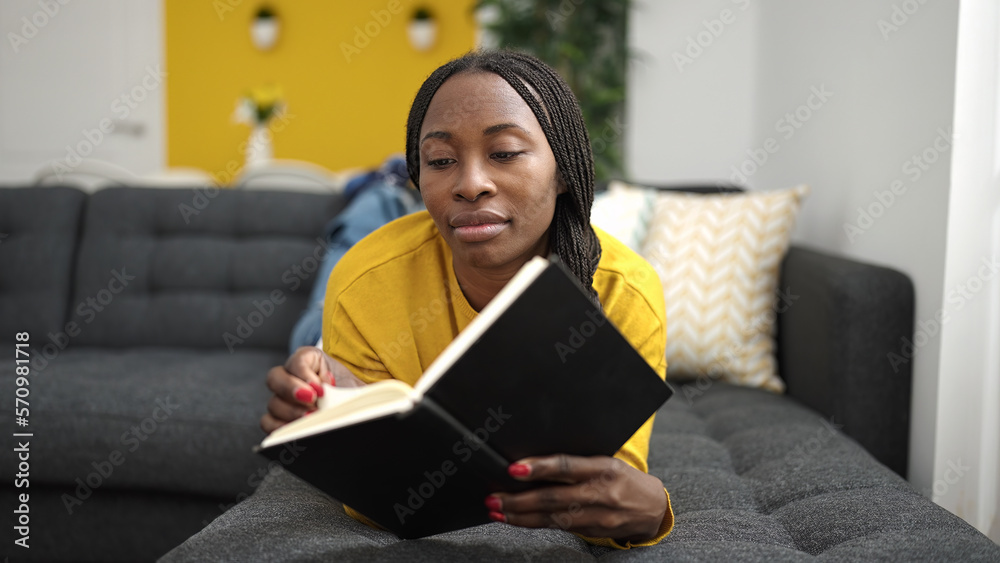 African woman reading book lying on sofa at home African woman reading book lying on sofa at home