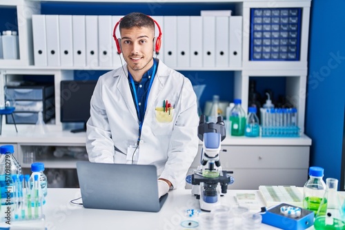 Young hispanic man scientist using laptop and headphones at laboratory