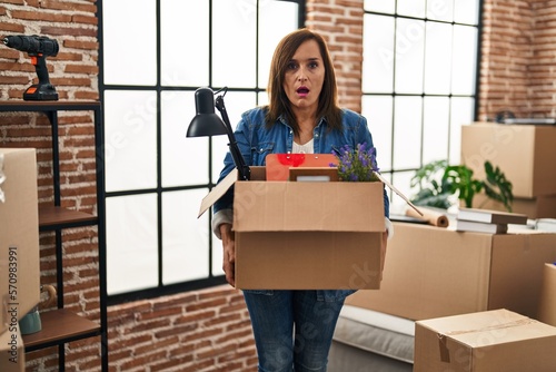 Middle age woman moving to a new home holding cardboard box afraid and shocked with surprise and amazed expression, fear and excited face. © Krakenimages.com