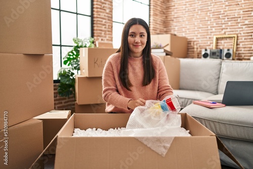 Young hispanic woman unpacking cardboard box sitting on floor at new home © Krakenimages.com