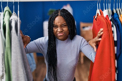 African american woman searching clothes on clothing rack skeptic and nervous, frowning upset because of problem. negative person.