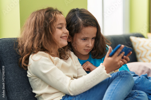 Two kids watching video on smartphone sitting on sofa at home