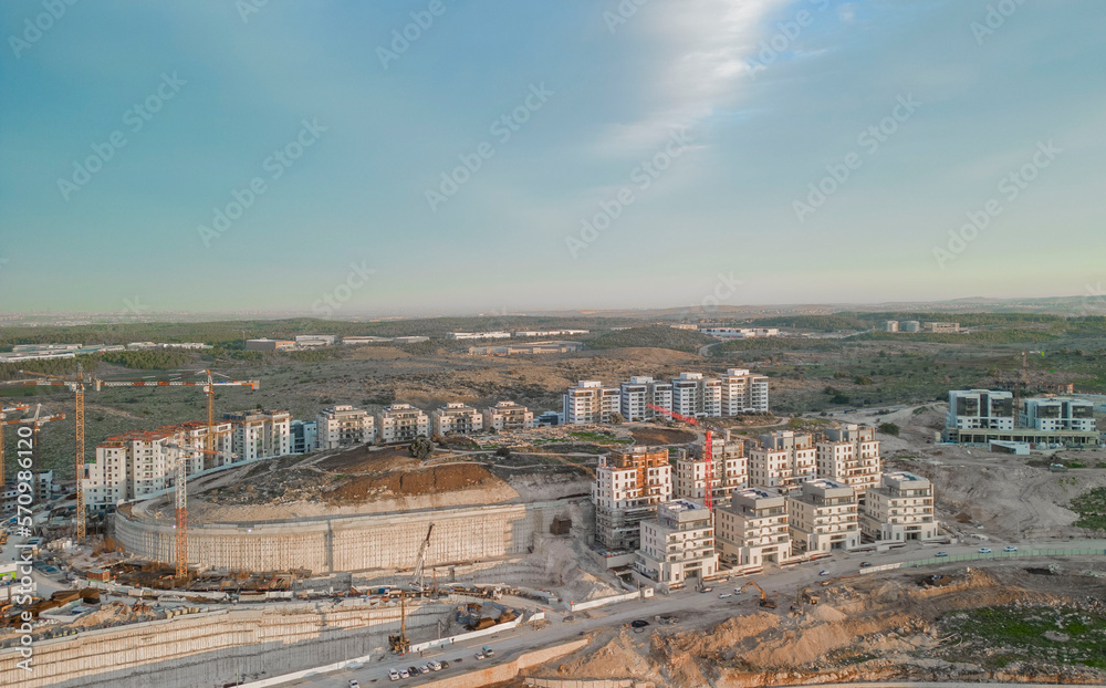 Modiin, Israel, January 11, 2023.Aerial view of the construction of a multi-story residential building and a large new residential area overlooking a green park with trees and a lawn next to