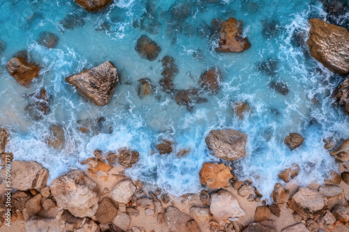 Aerial view of blue sea with waves, rocks and stones in clear water, rocky beach at sunny day in summer. Sardinia island, Italy. Beautiful seascape with sea coast, stones in azure water. Drone view