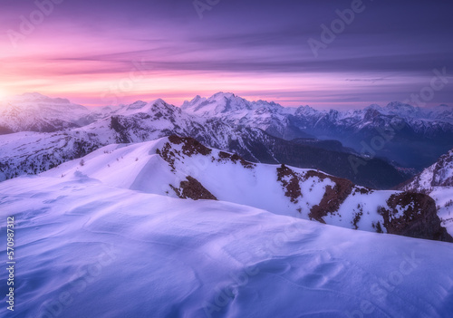 Fototapeta Naklejka Na Ścianę i Meble -  Snow covered mountains and colorful purple sky with clouds at sunset in winter. Beautiful wintry landscape with snowy rocks and hills at twilight. Scenery with alps at frosty evening. Alpine mountains